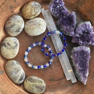 May include: A copper plate with a variety of crystals, including amethyst and selenite, and two bracelets with blue evil eye beads.