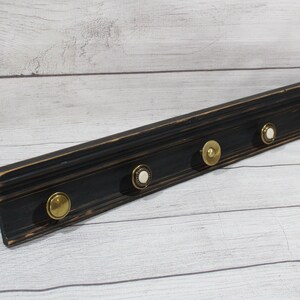 May include: Black wooden wall mounted coat rack with five gold and white knob hooks.