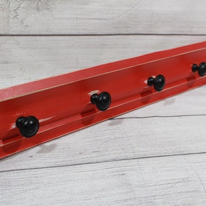 May include: Red wooden wall mounted coat rack with four black metal hooks.