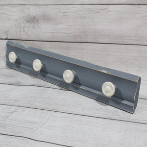 May include: A gray wooden coat rack with five white knob hooks. The rack has a distressed finish and is perfect for hanging coats, hats, or scarves.