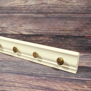 May include: White wooden shelf with four gold knob hooks. The shelf is on a wood background.
