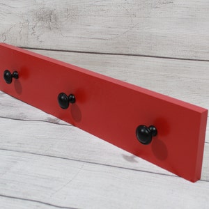 May include: A red wooden wall-mounted shelf with three black knob hooks.