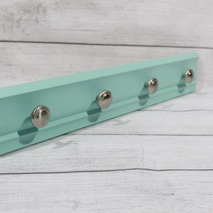 May include: A light blue wooden wall mounted key rack with four silver knob hooks.