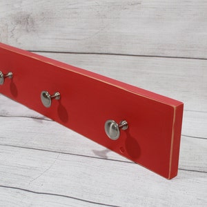 May include: Red wooden wall mounted key holder with three silver knob hooks.
