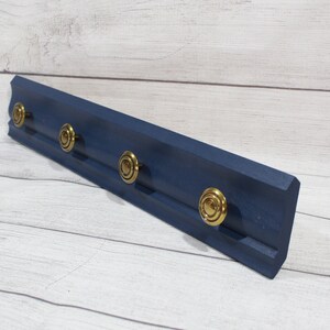 May include: A dark blue wooden wall-mounted coat rack with five gold knob hooks.