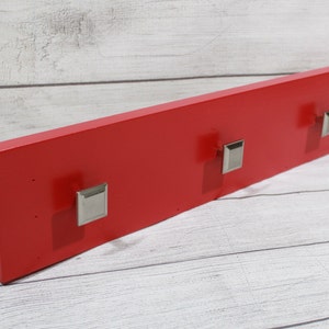 May include: A red wooden wall-mounted coat rack with three silver hooks.