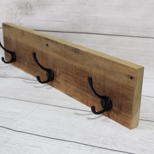 May include: A wooden wall-mounted coat rack with three black metal hooks. The rack is made of reclaimed wood with a natural finish.