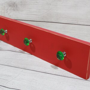 May include: Red wooden wall mounted coat rack with three green crystal knobs.