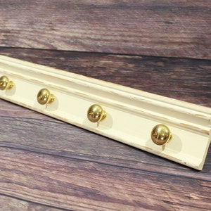 May include: A white wooden wall mounted coat rack with four gold knob hooks.