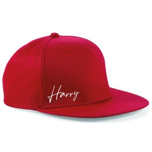 May include: Red baseball cap with a white cursive inscription that reads "Harry".