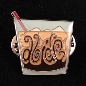 May include: A gold-colored pin shaped like a glass of iced coffee with a red straw. The coffee is brown with a swirl design and the text "dolce" is visible in the center.