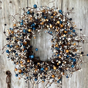 May include: A decorative wreath featuring a circular design with brown twigs and an assortment of colorful berries. The berries are in shades of blue, cream, and gold, creating a rustic and natural aesthetic. Perfect for seasonal home decor.