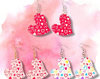 May include: Four pairs of heart-shaped earrings with a white background and a pattern of smaller hearts in various colors. The earrings are available in red, pink, yellow, and purple.