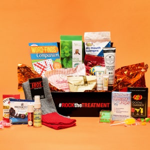 May include: A black box with the text "#ROCKtheTREATMENT" on the front. The box is filled with various items, including a word search puzzle book, a package of dry mouth lozenges, a tube of hand and body cream, a package of sinus soother, a package of natural tea, a package of socks, a bottle of hand sanitizer, a package of chocolate, a package of candy, a package of lollipops, and a package of jelly beans.