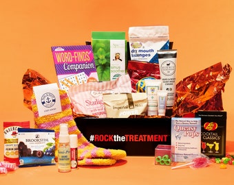 May include: A black box with the text "#ROCKtheTREATMENT" on the front. The box is filled with various items, including a book, socks, hand sanitizer, candy, and other small items.