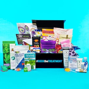 May include: A black box filled with various items, including a purple hat with the text "ROCK the TREATMENT", a pink and white bag with the text "Imperial Nuts", a blue and white box with the text "Queasy Pops", and a clear bottle with the text "LIND".