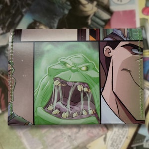 May include: A green and white wallet with a comic book style illustration of a ghost with sharp teeth and a man with a surprised expression. The wallet has a stitched edge.