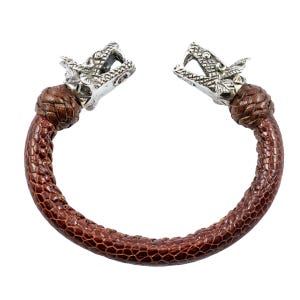 May include: A brown textured bracelet featuring a snake-like pattern along the band, finished with two silver-toned metal dragon head terminals at each end. The bracelet has a circular shape with an opening between the two dragon heads.