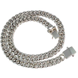Puede incluir: Un collar de cadena de eslabones de color plateado con un cierre seguro. La cadena está hecha de eslabones entrelazados, creando un accesorio audaz y elegante. El collar se muestra sobre un fondo blanco.