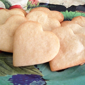 May include: A plate of heart-shaped cookies, baked to a light golden brown. The cookies are arranged in a cluster on a floral patterned plate.