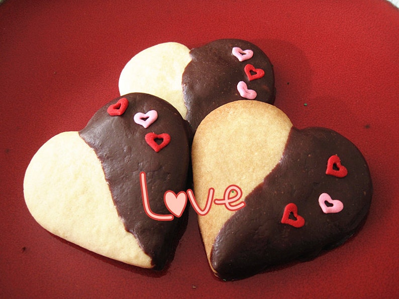 May include: Three heart-shaped cookies decorated with red and pink sprinkles. The cookies are half white and half dark chocolate. The word "Love" is written in pink and white on the cookies.