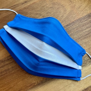 May include: A blue and white face mask with white elastic straps. The mask is folded in half and has a white lining.