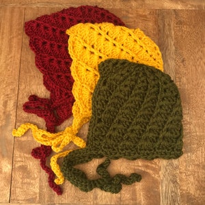 May include: Three crocheted hats in red, yellow and green. The hats are stacked on top of each other, with the red hat on the bottom, the yellow hat in the middle and the green hat on top.
