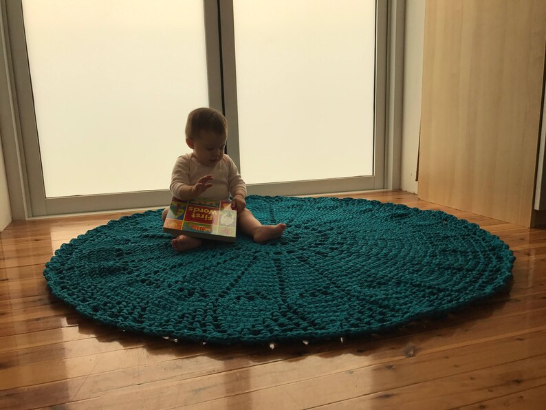 May include: A teal crocheted round rug with a child sitting on it reading a book titled "First Words".