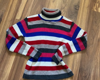 May include: A striped turtleneck sweater with red, white, blue, pink, and gray stripes. The sweater is made of a soft, knit fabric.
