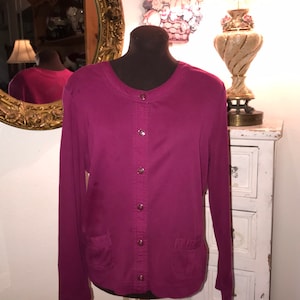 May include: A long-sleeved, button-up shirt in a deep burgundy color. The shirt has a round neckline and two pockets on the front.