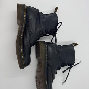 Puede incluir: Un par de botines de cuero negro con cierre de cordones. Las botas tienen un aspecto texturizado, suelas marrones y costuras amarillas. Estas botas clásicas son adecuadas para varios atuendos.