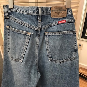 May include: A pair of light blue denim jeans with a red Wrangler label on the back pocket. The label says "Wrangler Premium Quality Comfort Guaranteed".