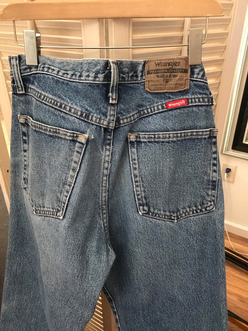May include: A pair of light blue denim jeans with a red Wrangler label on the back pocket. The label says "Wrangler Premium Quality Comfort Guaranteed".