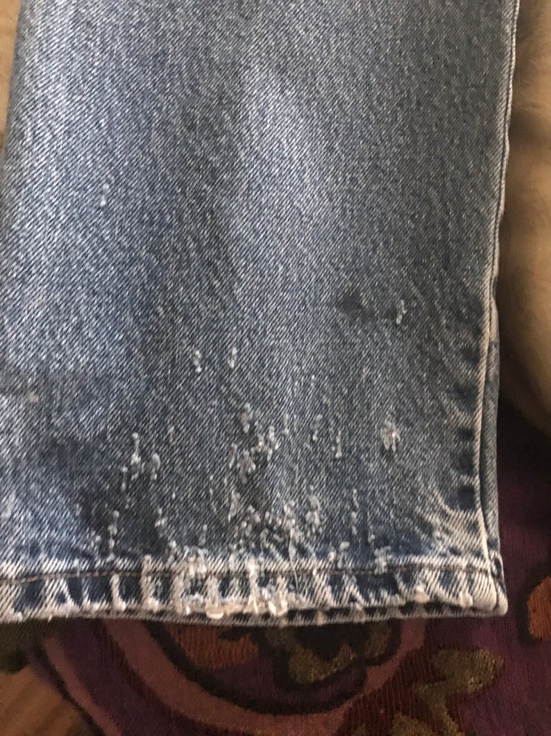 May include: Close-up of the bottom hem of a pair of blue denim jeans. The hem is frayed and worn, showing the white threads underneath.
