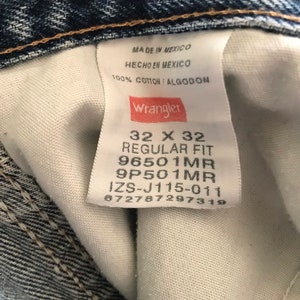 May include: A white Wrangler jeans tag with black text. The tag says "Made in Mexico", "Hecho en Mexico", "100% Cotton / Algodon", "Wrangler", "32 X 32", "Regular Fit", "96501MR", "9P501MR", "IZS-J115-011", and "672787297319".