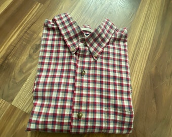 May include: A red, white, and blue plaid button-down shirt folded on a wooden surface.