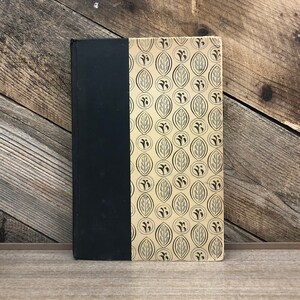 Peut inclure: Un livre relié en noir et or avec un motif de feuilles répété sur la couverture.