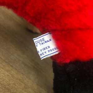 以下が含まれることがあります： 「House of Taiwan、All Fiber、Disney Prods.」と書いてある青いラベルが付いた、赤と黒のぬいぐるみ
