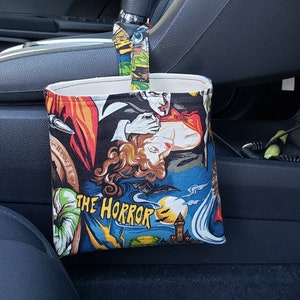 Op de afbeelding: Een stoffen auto-afvalzak met een vintage horrorfilmafbeelding. De tas heeft een kleurrijke print met afbeeldingen van vampiers, vleermuizen en een spookkasteel. De tekst "THE HORROR" staat erop.