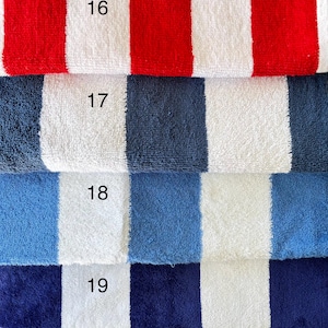 Op de afbeelding: Vier opgestapelde badhanddoeken van badstof met verticale strepen in rood, antracietgrijs, middenblauw en marineblauw, elk afgewisseld met wit. De handdoeken zijn voorzien van de nummers 16, 17, 18 en 19, in het zwart gedrukt op de witte banen.