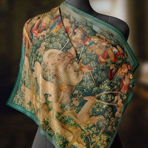 May include: A green silk scarf featuring a tapestry print of a unicorn hunt. The print depicts a white unicorn, a group of hunters, and a forest scene.
