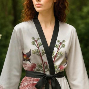 May include: A gray silk robe with a black sash and a floral print featuring hummingbirds and red flowers. The robe has long sleeves and a V-neck.