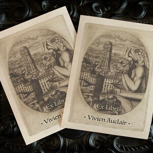 May include: Two vintage bookplates featuring a black and white illustration of a gargoyle overlooking a city skyline. The text on the bookplates reads "Ex Libris Vivien Auclair".