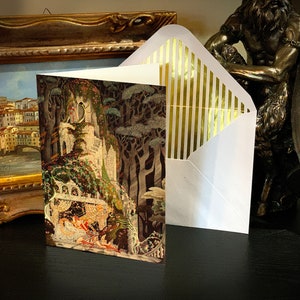 May include: A white envelope with gold stripes on the flap. The envelope is closed and has a card inside. The card features a colorful illustration of a castle in a forest.