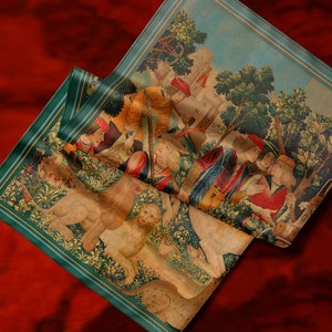 May include: A tapestry depicting a scene from the hunt of the unicorn. The tapestry features a lion, a unicorn, and several people in medieval clothing. The tapestry is folded in half and has a green border.