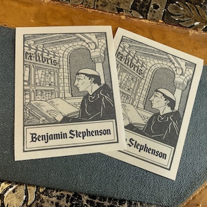 May include: Two monochrome Ex Libris bookplates depicting a monk reading in a library. The bookplates display the text "Ex Libris" and the name "Benjamin Stephenson". They are set against a textured background, with a leather-like appearance.
