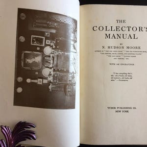 May include: An open book titled "The Collector's Manual" by N. Hudson Moore. The book features a sepia-toned illustration and text. Published by Tudor Publishing Co. in New York. The book's pages are off-white.