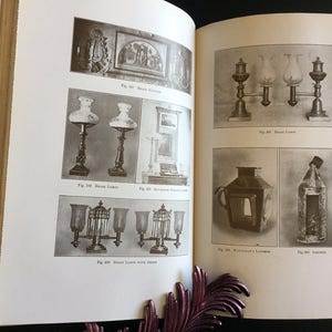 May include: Open book with black and white illustrations of antique lamps and lanterns. The lamps include table lamps and hanging lamps. The book is open to two pages with multiple images and text.
