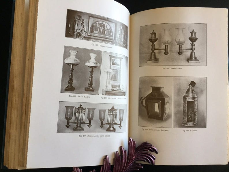 May include: Open book with black and white illustrations of antique lamps and lanterns. The lamps include table lamps and hanging lamps. The book is open to two pages with multiple images and text.