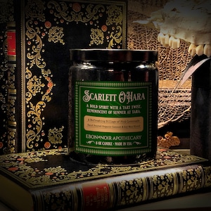 Peut inclure: Un bocal de bougie vert avec un couvercle noir et une étiquette verte qui indique "Scarlett O'Hara" avec le texte "Un esprit audacieux avec une touche acidulée. Évoquant l'été à Tara. Un mélange rafraîchissant de limonade rose. Cire de soja et de noix de coco biologique coulée à la main. Ebon Noir Apothecary Bougie de 8 oz - Fabriquée aux États-Unis."